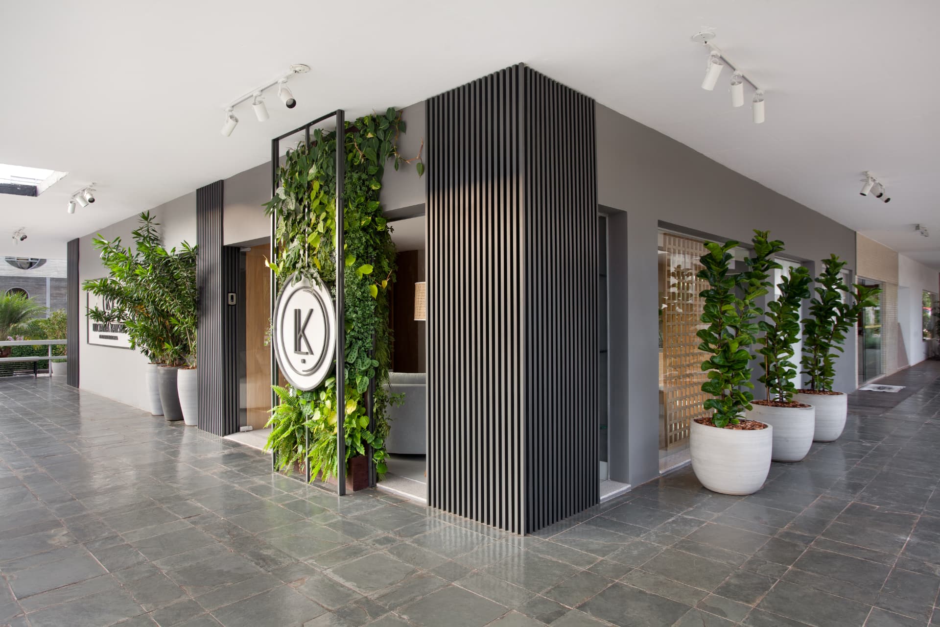 Fachada de la Clínica Odontológica L | K con jardín vertical, panel de listones oscuro y macetas blancas sobre piso de piedra